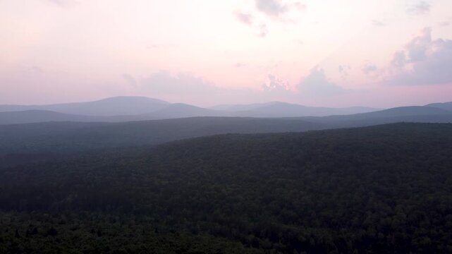 Aerial sunset video of rolling green mountain ridges and dense forest in Maidstone, Vermont.