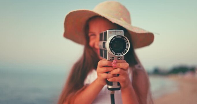 Little girl with old vintage camera making photos of sea waves and beach. Young photographer. 