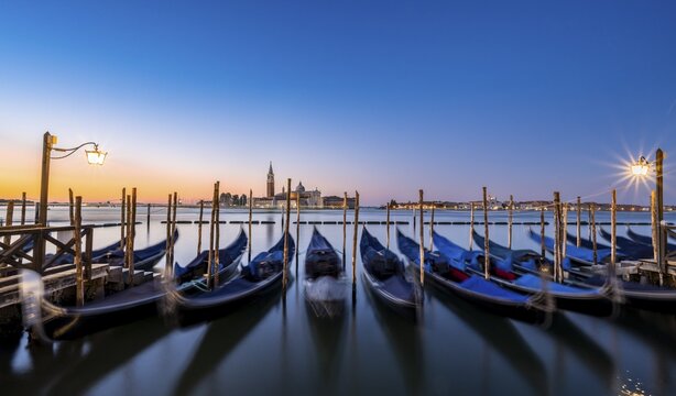 Venetian gondolas, boat dock at St Mark's Square, church of San Giorgio Maggiore in the background, long exposure at sunrise, Venice, Veneto, Italy