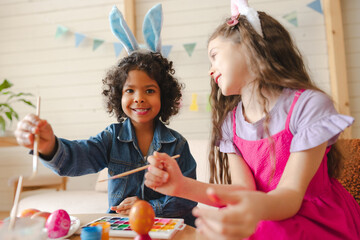 Happy diverse children decorating Easter eggs, wearing bunny ears, celebrating spring