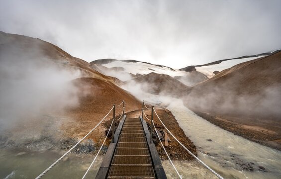 Bridge over steaming stream between colourful rhyolite mountains with snowfields, Hveradalir geothermal area, Kerlingarfj&ouml;ll, Icelandic highlands, Iceland
