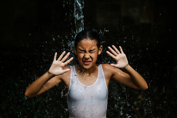 Fototapeta premium Young girl recoils from splashing water in a white tank top child