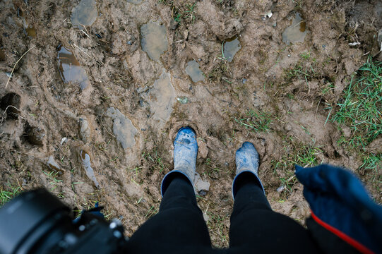 A photographer standing in a field with blue boots sinking in the mud
