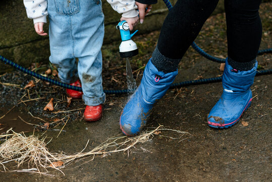 Mother and daughter washing their muddy boots with a hose on a farm
