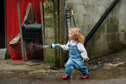 Little toddler girl playing with a hose and water on a farm