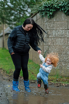 The joy and freedom of a mother and daughter jumping in a muddy puddle