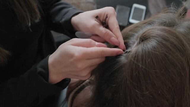 Professional hair stylist hands preparing a small strand of hair for the extension process in a beauty salon