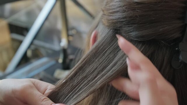 Professional stylist separating strands of long brown hair for hair extension procedure in a beauty salon close up