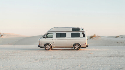 Vintage camper van parked on sandy desert landscape during sunset
