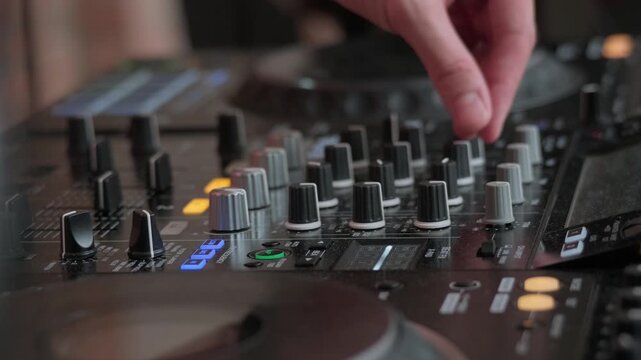 Close-up of a hand adjusting a fader on a professional DJ mixer with illuminated buttons