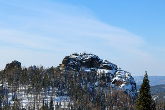Tall snow covered rock formation with pine trees in Krasnoyarsk Pillars national park. Winter landscape with natural Siberian mountain forest.