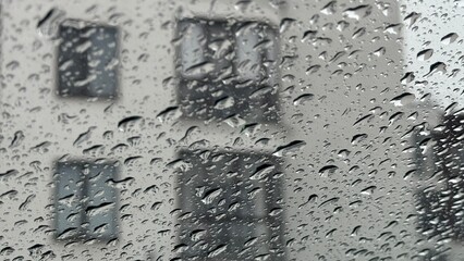 Macro shot of heavy rain drops on transparent glass. Heavily blurred windows of a city apartment building in the background during wet weather. © AndreyZayats