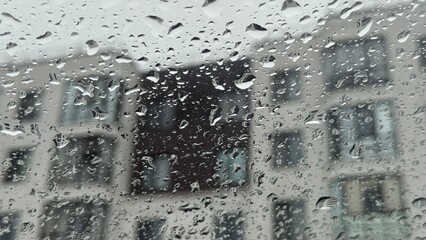Water droplets trickling down a windowpane during a rainstorm. Blurred silhouette of a contemporary apartment block against a grey overcast sky. © AndreyZayats