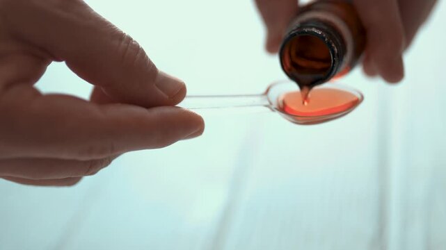 Man pouring liquid cough syrup into a spoon, medication dosage and healthcare concept.