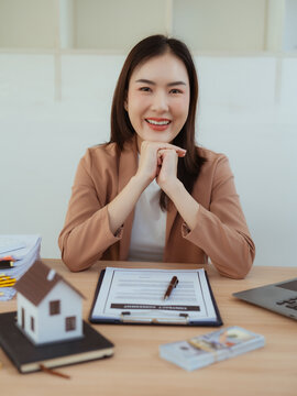 A real estate agent or manager sits at a desk in a modern office, working on a laptop with miniature house models.