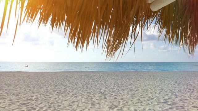 White sand tropical Caribbean beach of Varadero, Cuba as seen from under a palm frond umbrella. Gradual cloud cover, from sunny to overcast.