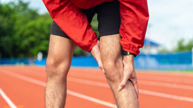 Close up young asian runner athlete with muscle pain. Man massaging Stretching, trauma injury while jogging outdoors. Fitness male sprain severe pain stretch pull. Leg muscle cramp calf sport.