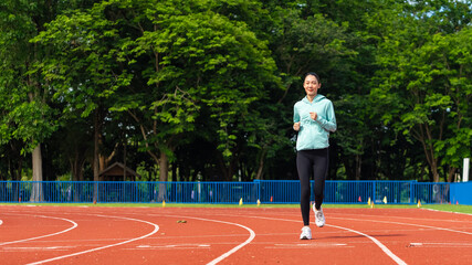 Fototapeta premium Young Asian women are exercising with outdoor running with a running track background in the morning. Concept healthy running and outdoor exercise, Tracking shot,