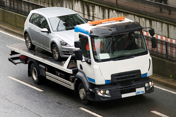 towing  truck car wrecker transporting a broken down car working  in city street