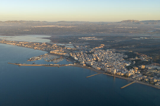 Aerial view of sun-kissed buildings sprawl along the coastline, meeting the vast azure sea, with mountains fading into the horizon, Santa Pola, Valencian Community, Spain.