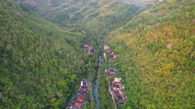 Aerial drone footage of a hidden local village in the middle of a vast forest and mountains valley, with the touristic Maron river, in Pacitan regency, Java island, Indonesia