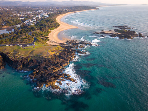 Aerial view of the rugged headland meets the inviting sands of the beach, where the deep blues of the ocean contrast with the golden shoreline, Sawtell, New South Wales, Australia.