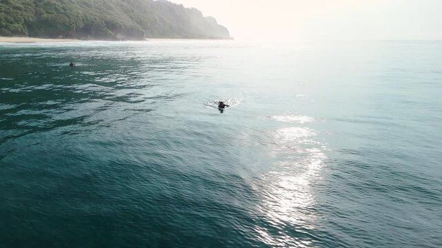 Surfer woman rowing on surfboard in ocean with coastal landscape. Drone shot
