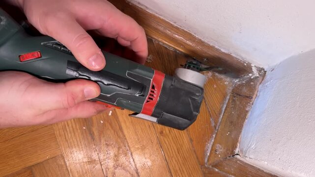 Hands using oscillating multitool to cut baseboard corner, home renovation carpentry detail for remodeling and repair, focused practical mood for DIY and maintenance
