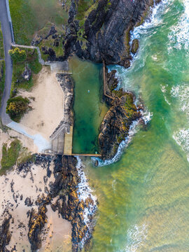 Aerial view of the contrasting turquoise ocean meeting the rugged, dark cliffs and sandy beach, defining the coast, Sawtell, New South Wales, Australia.