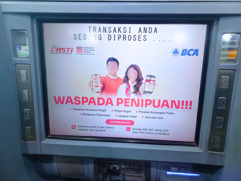 Denpasar, Indonesia - August 20, 2025: A warning message about illegal investments and fraud displayed on a BCA automated teller machine screen.