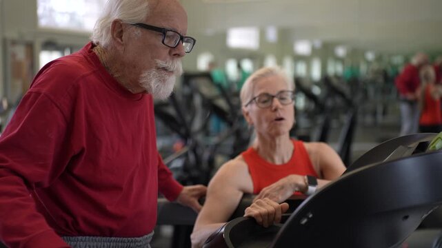 Elderly man engages in workout with trainer at gym, focusing on fitness and strength training for seniors.