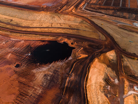 Aerial view of dark water reflecting the sky amidst terraced earth and industrial landscape, contrasting with the ochre ground, Aluminium Refinery, Western Australia, Australia.