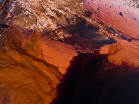 Aerial view of stark, contrasting industrial landscape reveals rust-colored earth bleeding into dark, shadowed pools, Aluminium Refinery, Western Australia, Australia.