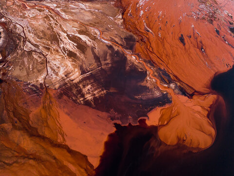 Aerial view of stark, rust-colored earth meets deep, dark pools, creating a mesmerizing contrast of textures and tones, Aluminium Refinery, Western Australia, Australia.