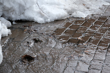 Snow melting and puddles forming on a cobblestone sidewalk in spring