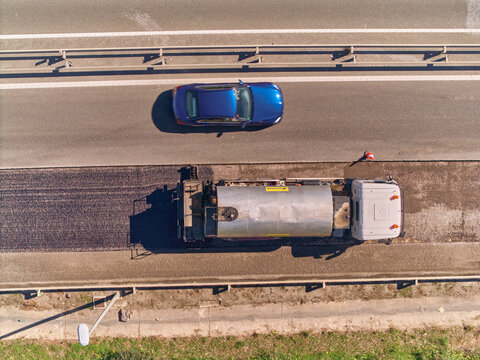 Aerial view of a blue car passing a Tack Distributor or bitumen truck while on a soon to be paved roadlane, on highway A-7, Estepona, Andalusia, Spain.