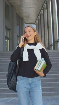Portrait of good-looking in high spirits stylish 20-aged blondie which studying in university and talking on mobile while going down the stairs when exiting the campus building