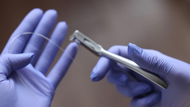 Extreme close up of orthodontist using pliers to handle thin archwire during braces adjustment. Gloved hands demonstrate precise control and careful fixation of orthodontic wire in clinical setting.