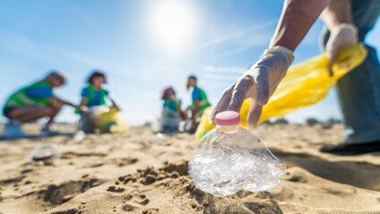 Obraz premium Group of eco volunteers picking up plastic trash on the beach - Activist people collecting garbage protecting the planet - Ocean pollution, environmental conservation and ecology concept