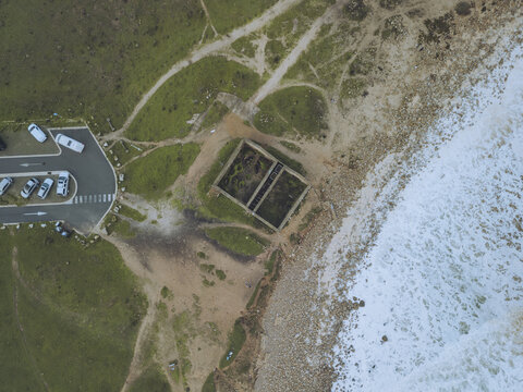 Aerial view of the stark contrast between the rugged coastline meeting the restless ocean, and the geometric man-made structure along the Boca do Rio, Budens, Faro, Portugal.
