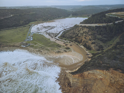 Aerial view of the meeting of the river and the sea, the waves crashing against the shore, Boca do Rio, Budens, Faro, Portugal.