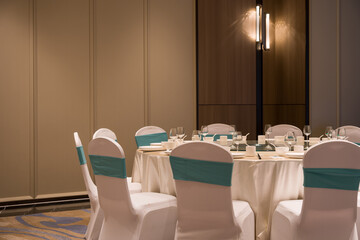 Elegantly set round banquet table in hotel conference room with white chair covers and teal satin...