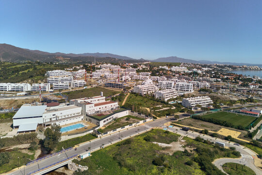 Aerial view of gleaming white residential complexes nestle amidst verdant hills, kissed by the azure sea, creating a striking contrast of urban elegance and natural beauty, Estepona, Andalusia, Spain.