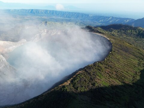 Aerial view of a volcano crater rimmed with green vegetation and shrouded in ethereal mist, a breathtaking landscape, Java, Java, Indonesia.