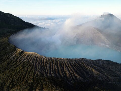 Aerial view of the Ijen volcano complex with its turquoise crater lake surrounded by the rugged terrain and misty atmosphere, Java, Java, Indonesia.