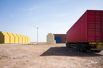 Red container truck parked in a storage yard with wind turbine in the background