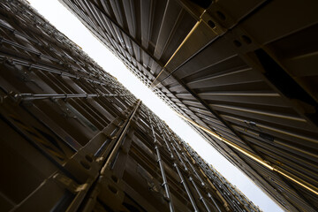 Fototapeta premium Upward view of stacked shipping containers forming a narrow sky gap with structural lines