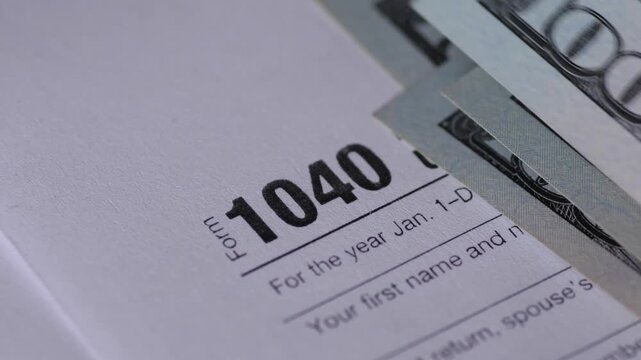Close up of U.S. Tax Form 1040 with hundred dollar bills being placed on top. Concept of tax payment, tax refund, and financial wealth management
