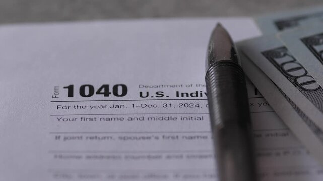 Close up of 1040 tax return form with a pen and a stack of dollar cash. Concept of filling out tax documents, financial audit and government payments