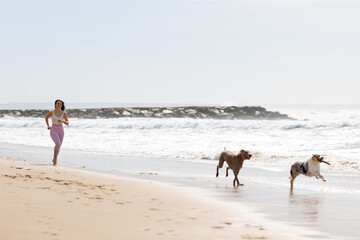 Woman running with dogs on sandy beach